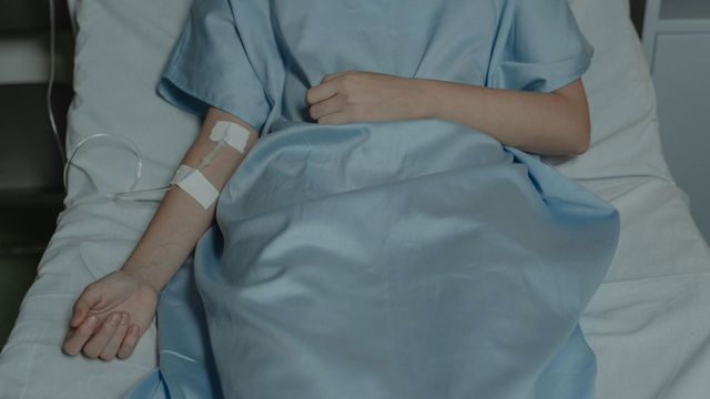 A patient in a hospital gown receives treatment through an IV. 