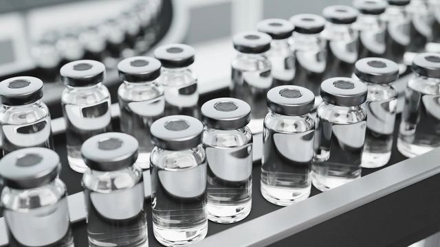 Clear glass vials filled with a colourless liquid sit on a conveyor belt. 