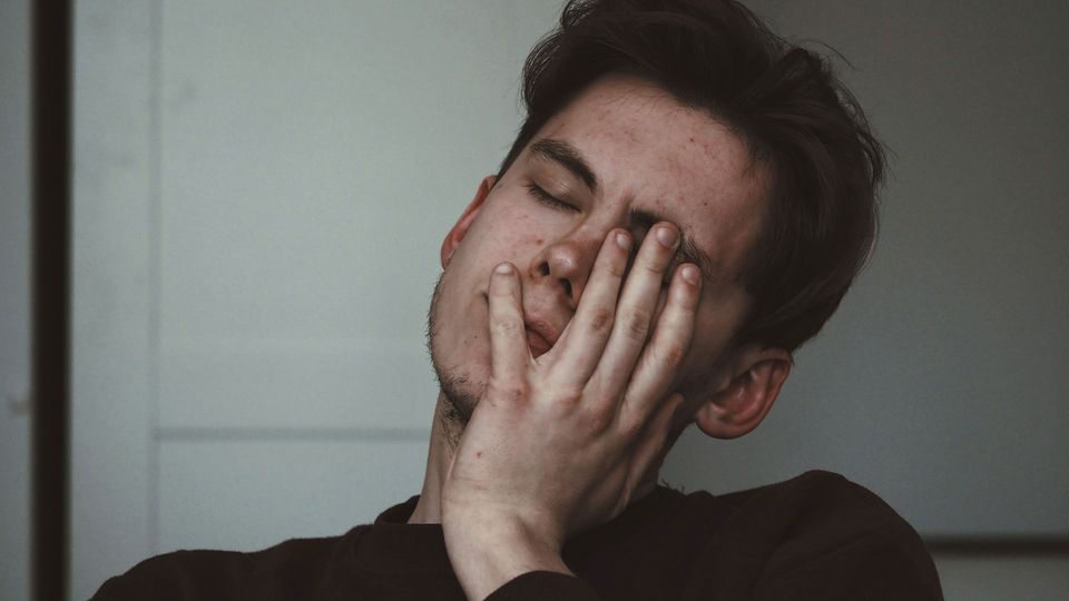 A young man holds a hand to on side of his head.