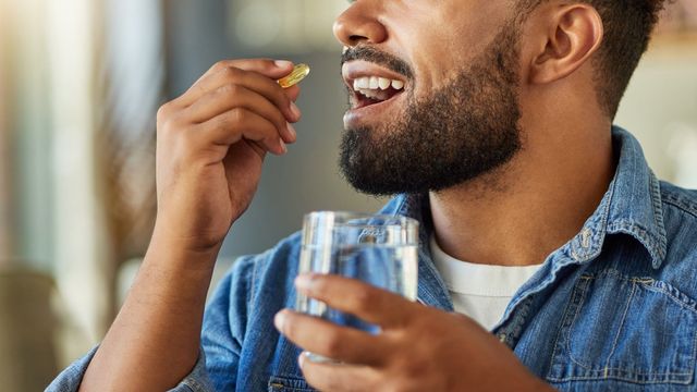 A man holding a glass of water and a vitamin to his mouth. 