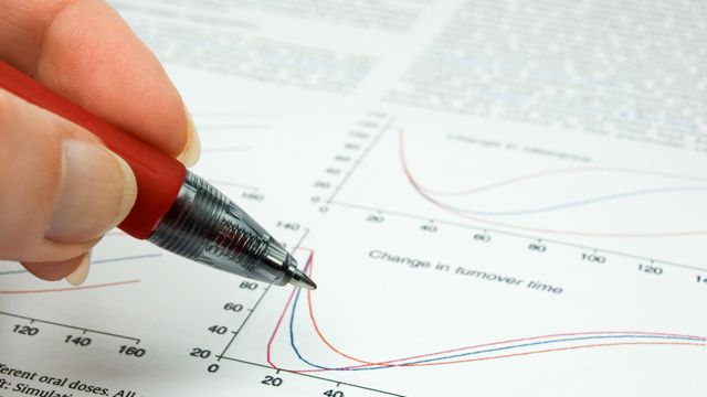 A person's hand holding a pen poised over a graph in a scientific paper. 