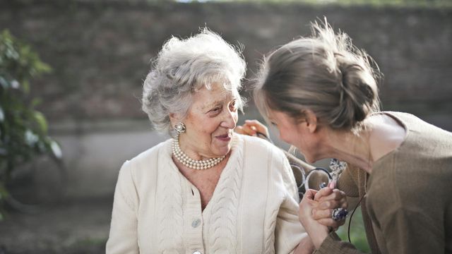 An older mother and daughter hold hands while smiling. 