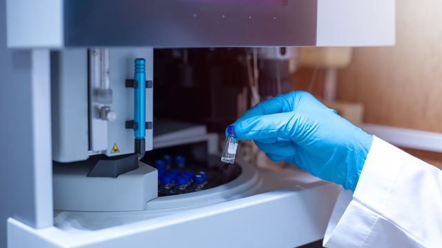 A gloved hand placing a vial inside an LC-MS instrument. 