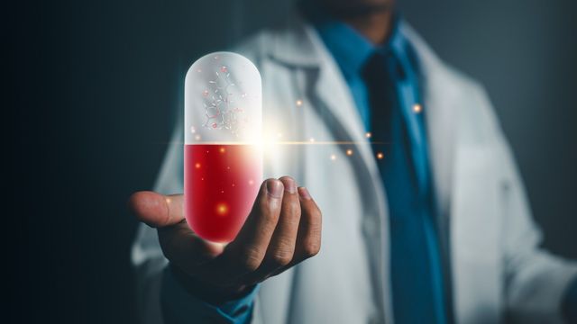 Someone in a lab coat holding up a red and white capsule. 