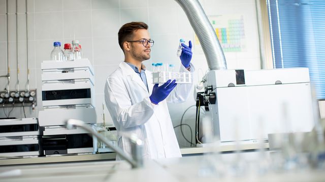 A man in a lab coat holding a tube rack in a laboratory. 