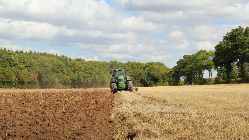 A green tractor halfway through ploughing a field.