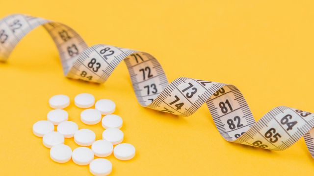 Small white pills next to a curling tape measure on a yellow background. 