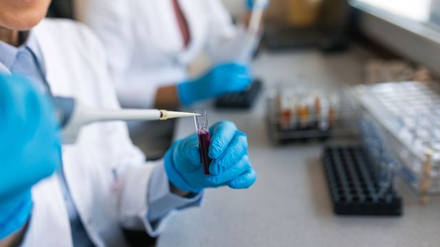 A scientist pipetting into a tube. 