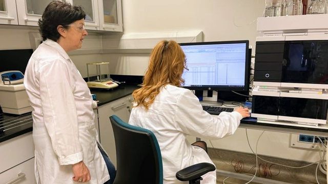 Two scientists wearing lab coats in a lab looking at data on a computer screen. 