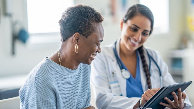 Female doctor and patient seated, smiling and looking at a tablet. 