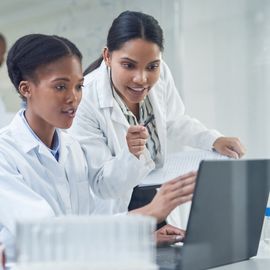 Two young female scientists work on a laptop. 