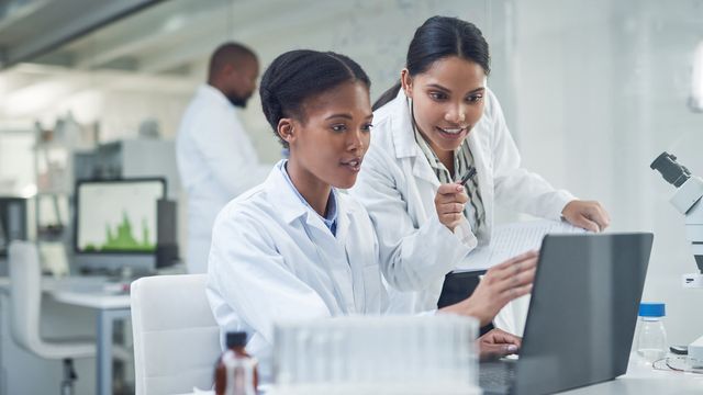 Two young female scientists work on a laptop. 