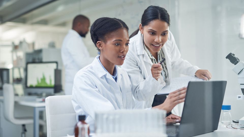 Two young female scientists work on a laptop.