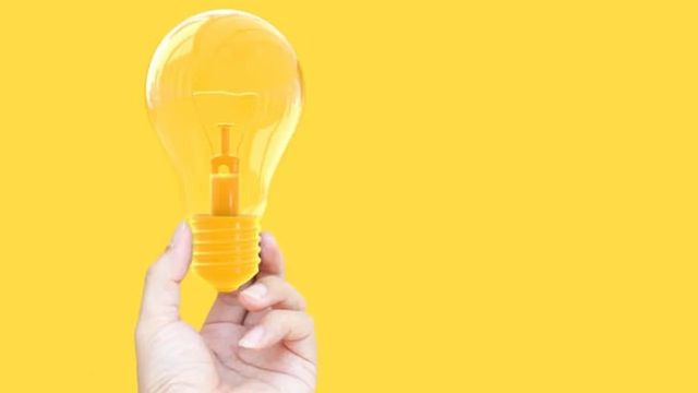 hand holding lightbulb on yellow background 