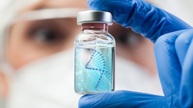 A scientist holding up a vial containing an image of a DNA double helix. 